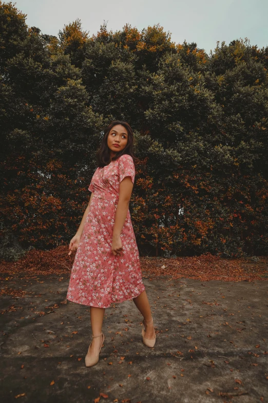 a young woman in a red dress standing by a hedge