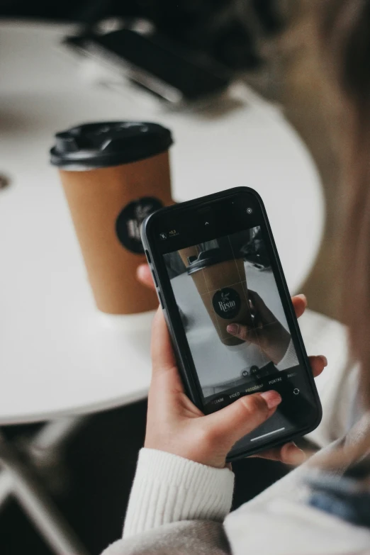 a woman is holding her phone with the image of a cup