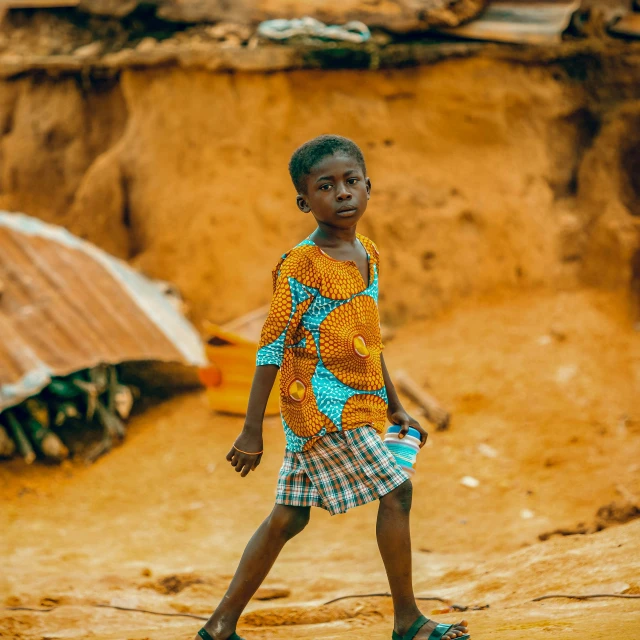 a  wearing a colorful outfit standing outside in front of muddy houses