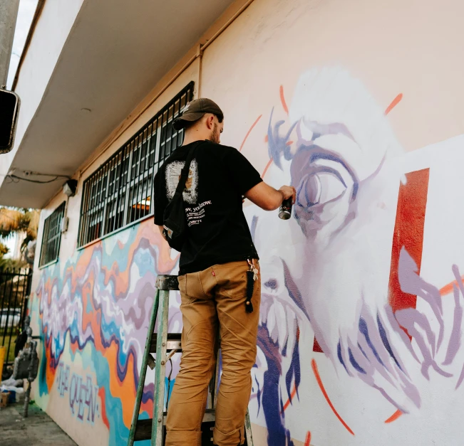 a man on a small ladder painting on a wall