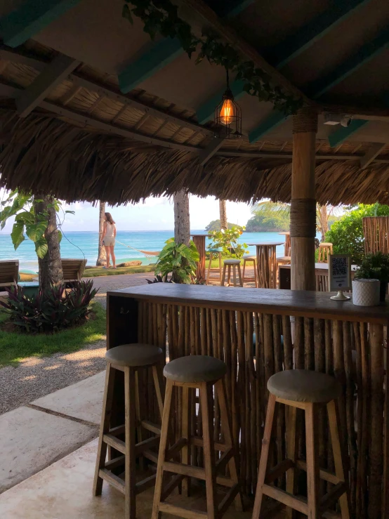 an outside bar with stools sitting under a straw hut