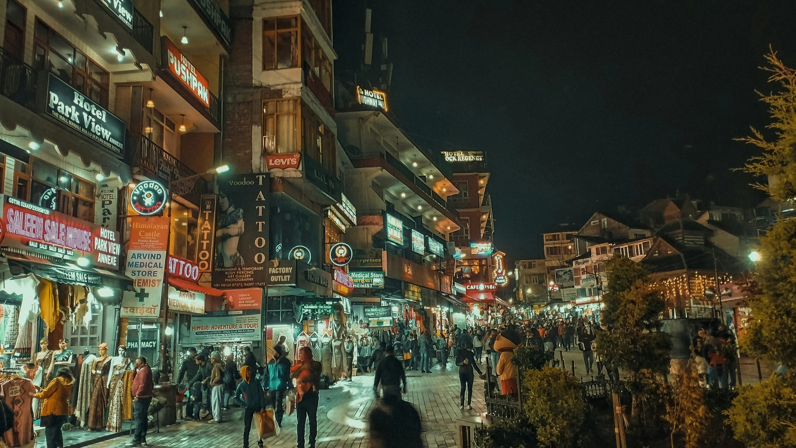 a crowded sidewalk at night in a shopping district