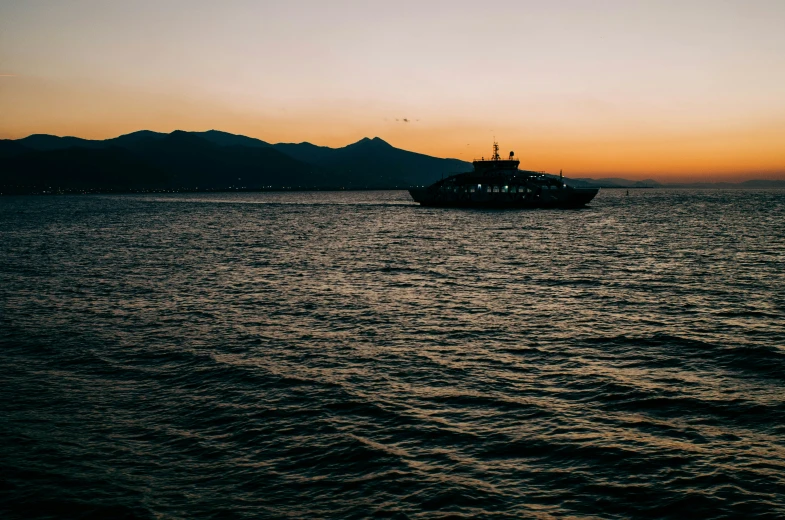 a ship at sea during sunset with a hill in the distance