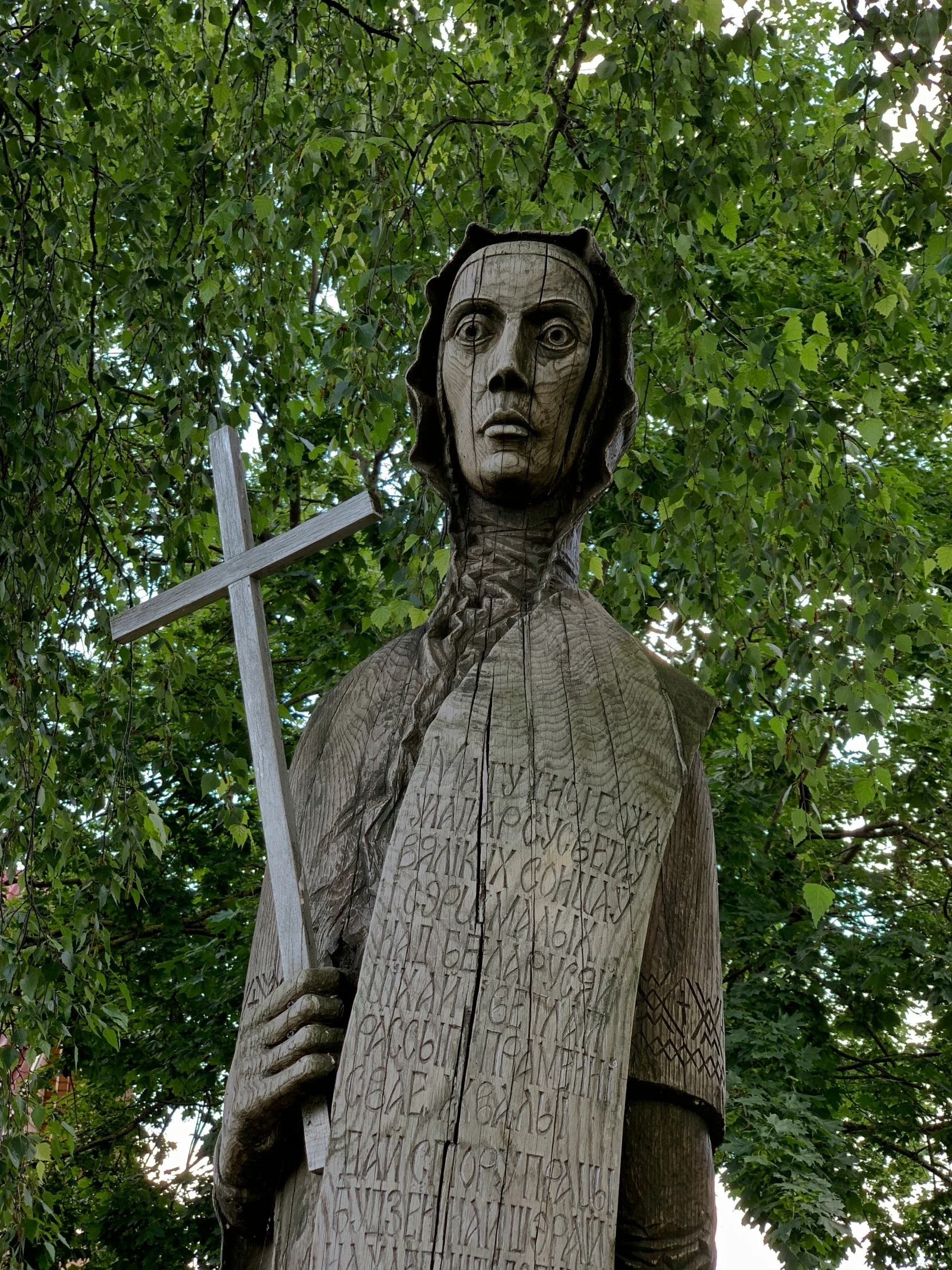 a statue of a man holding a cross behind a tree