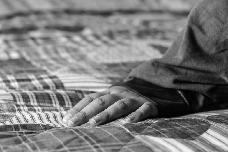 a hand resting on a blanket that is laying on a bed