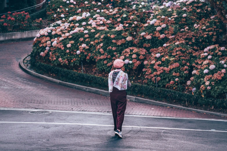 a person walking down the road in front of flower bush