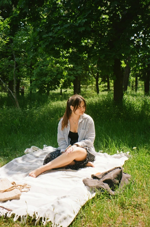 a woman is sitting on a blanket on the grass