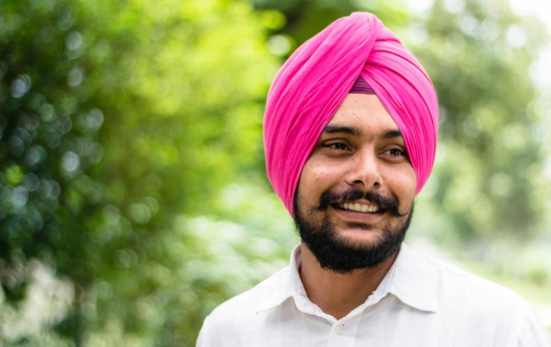 an indian man in a bright pink turban smiles while wearing his turban