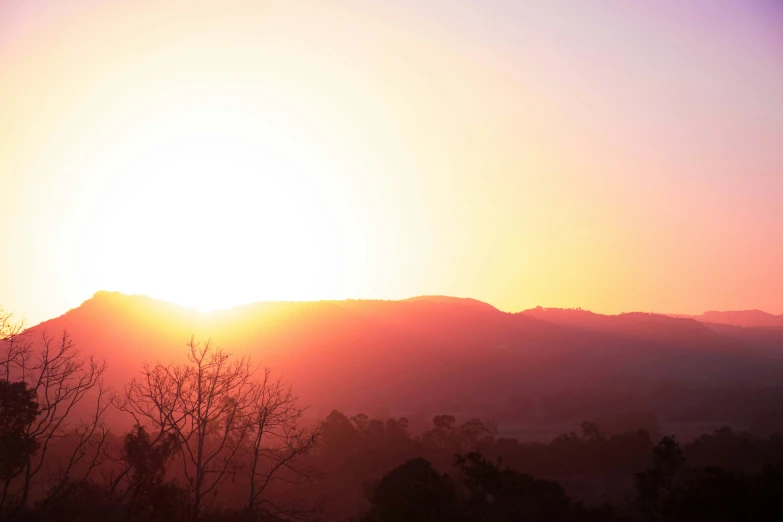 the setting sun over a hill with trees in the foreground