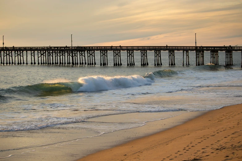 waves come up onto a beach as the pier extends into the water