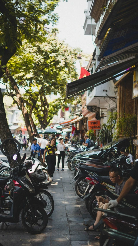 people walk past a street lined with parked motorcycles