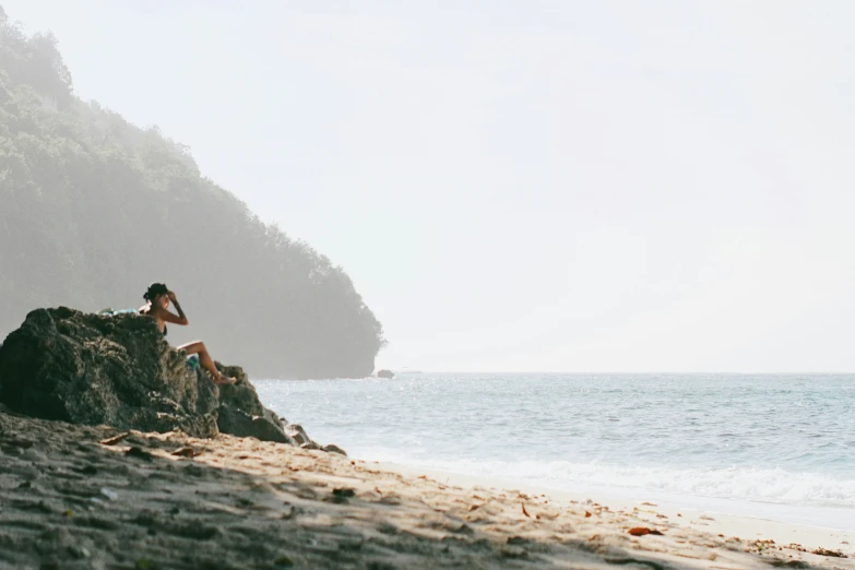 a person sitting on a rock in the sand at the beach