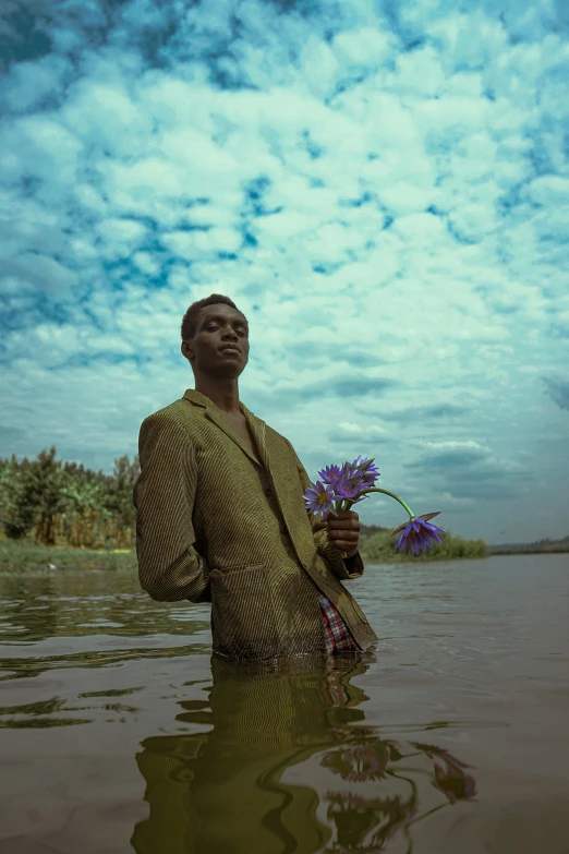 a man standing in a body of water holding a purple flower