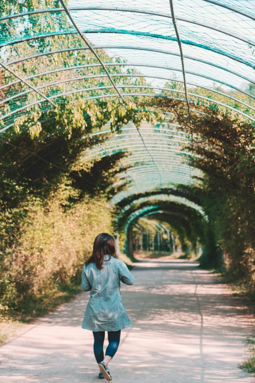 woman in gray jacket walking down an alley between trees