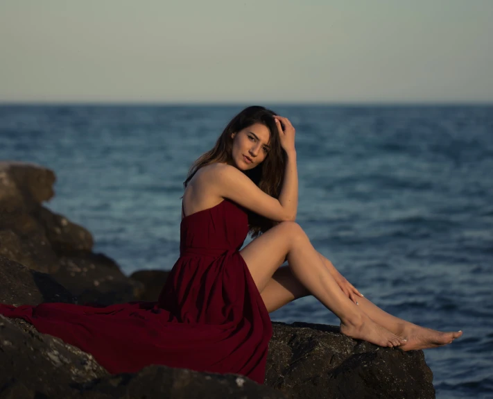 a woman sits on rocks looking out to sea