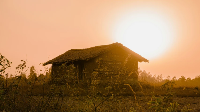 an abandoned stone building in the foreground with the sun behind it