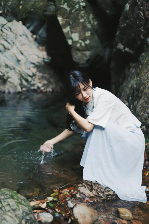 a woman reaching out from a creek in front of a rock wall