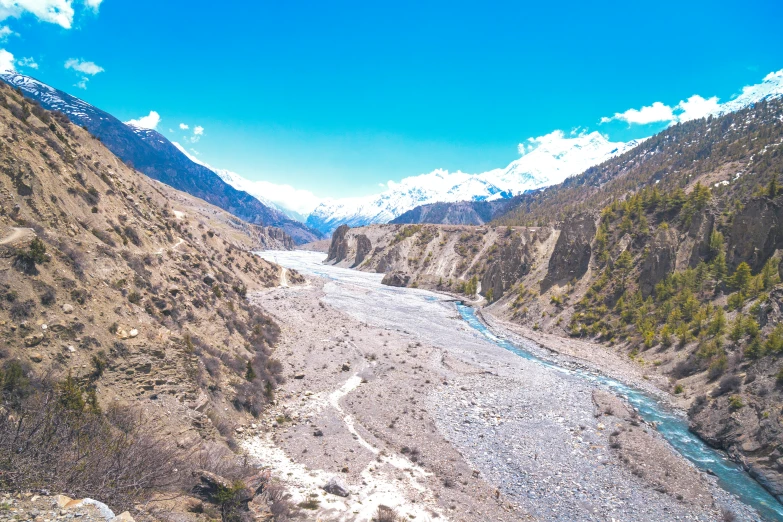 a mountain stream next to the mountains with snow