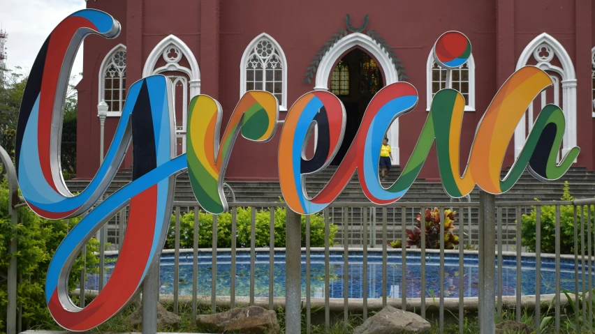 a sign with a red building in the background and a blue pool