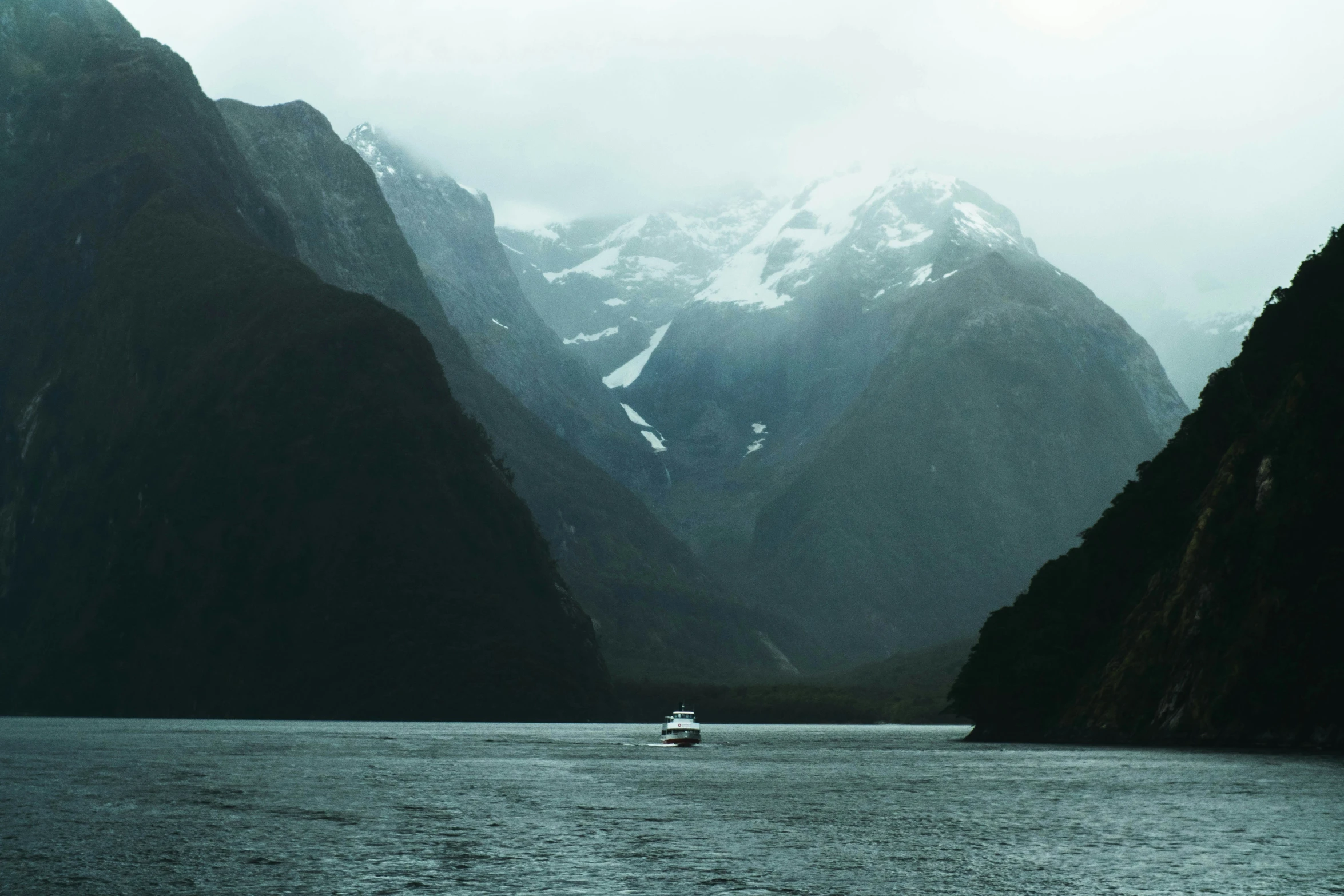 a boat sails through a mountainous lake in the rain