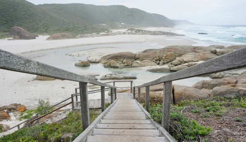 stairs leading to a sandy beach with boulders in the background