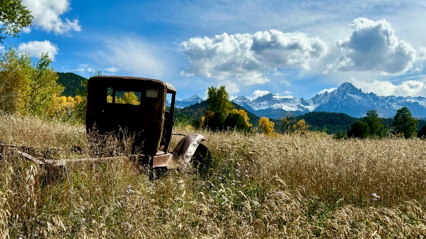 an old car sits in a field of tall grass