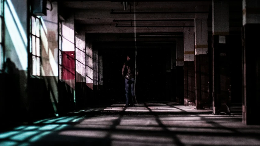 man stands alone in an empty hallway with shadows