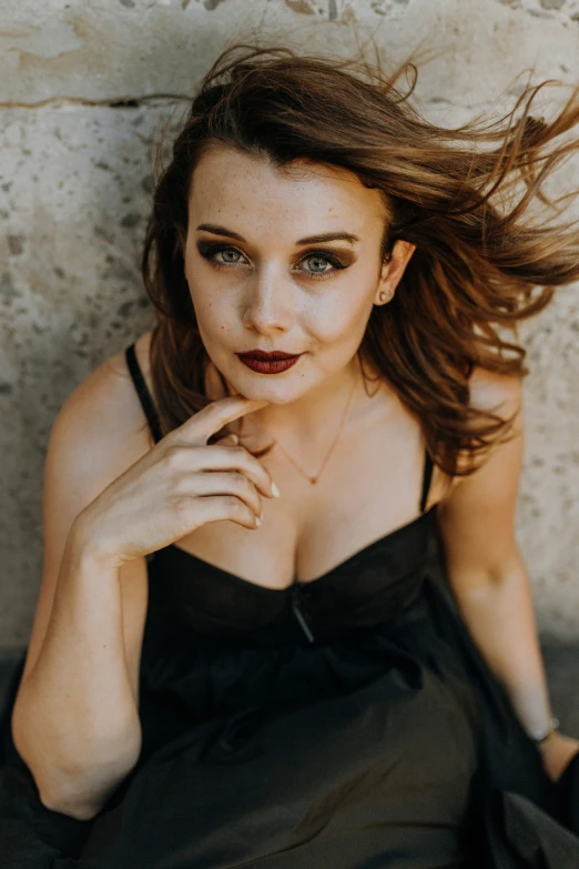 a woman sitting against a wall with her hand on her chin