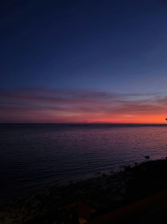 a person sitting next to the ocean at sunset