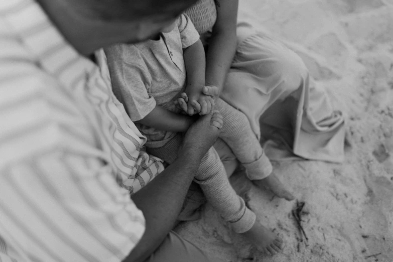 an adult holds a child on her lap in the sand