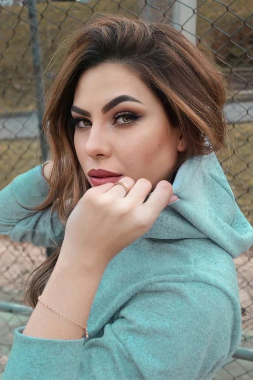 a beautiful young woman leaning on a fence wearing a green coat