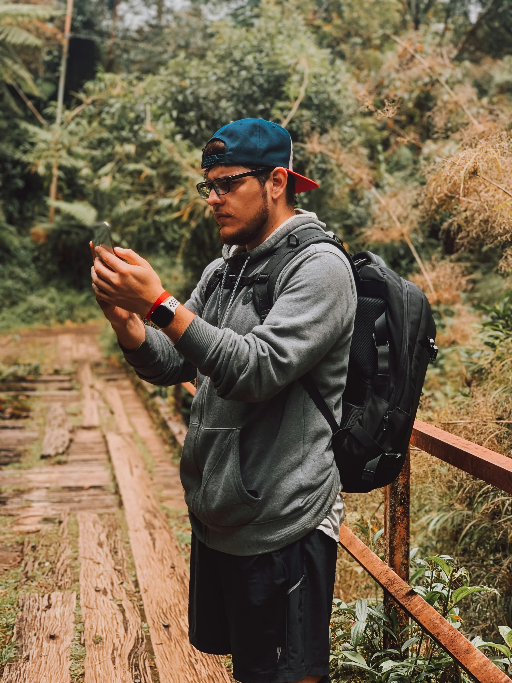 man with backpack standing on footpath using cell phone