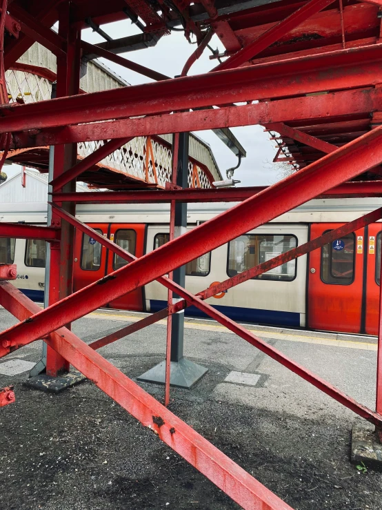 a red metal fence at a train station as a train approaches