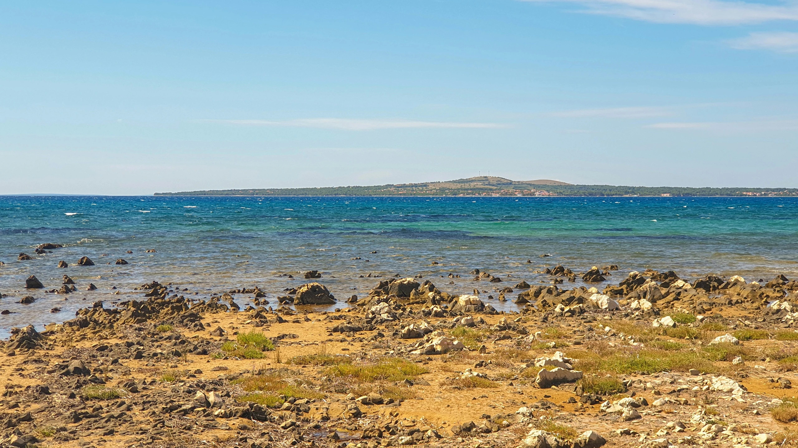 a grassy shore line with rocks on top and some water in the middle