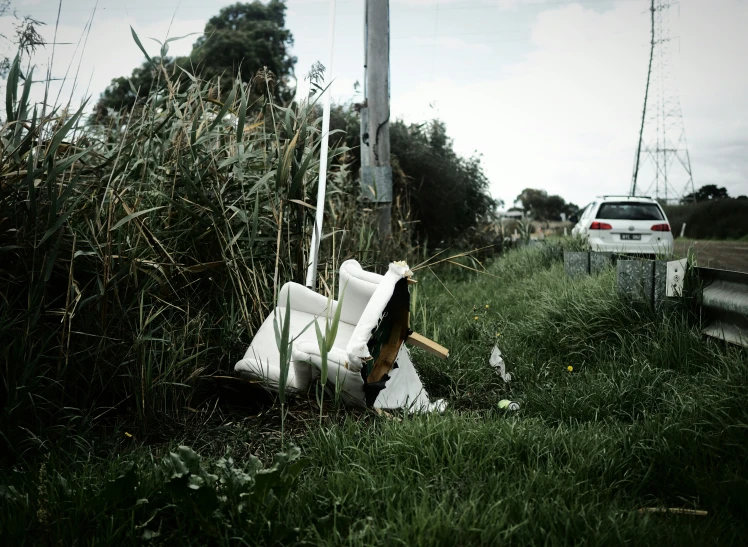 a broken up chair in the grass with a car parked behind