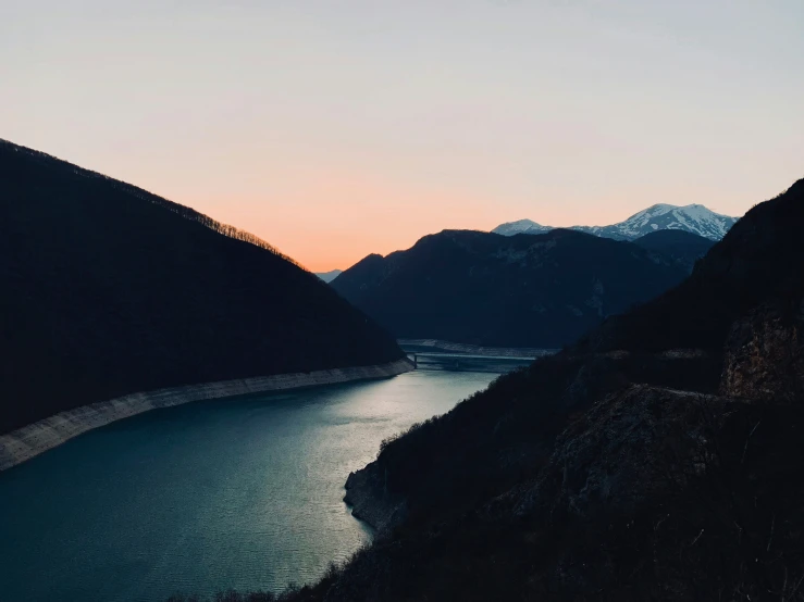 a dark scene with mountains, a body of water and a road