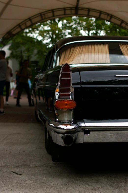 a black, old fashioned car parked under a canopy