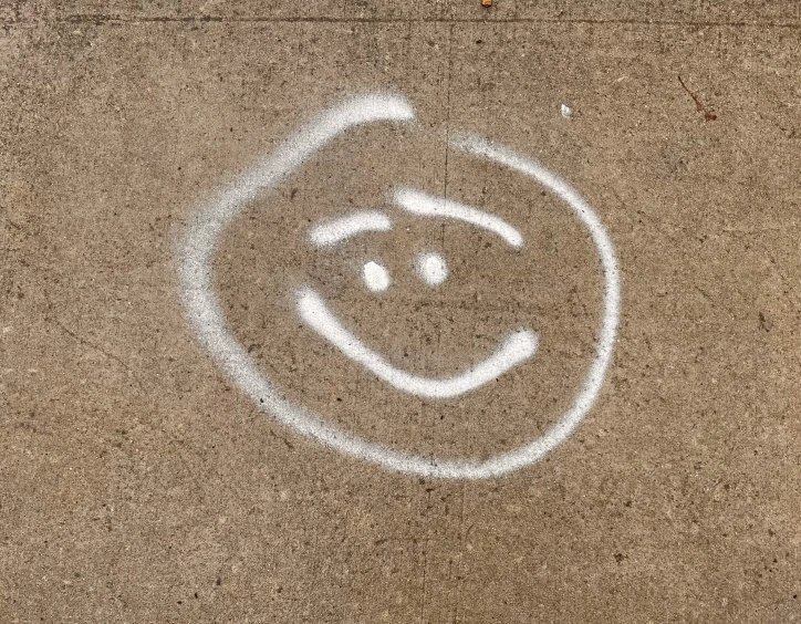 the face of a smiling person with eyes and mouth drawn in white chalk
