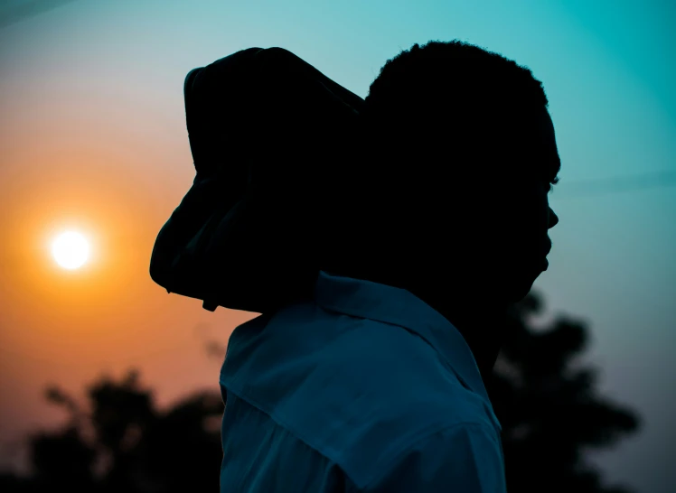 man wearing a headscarf over his head, while the sun sets in the background