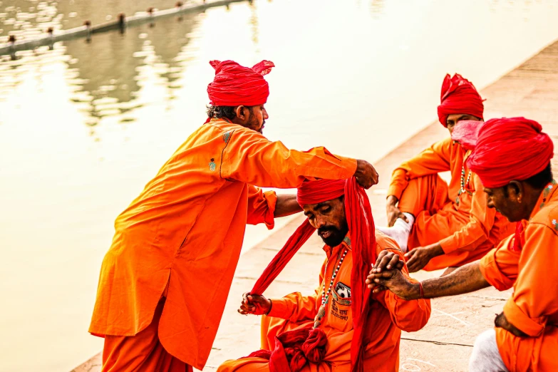 several men dressed in orange are doing soing at the edge of a pond