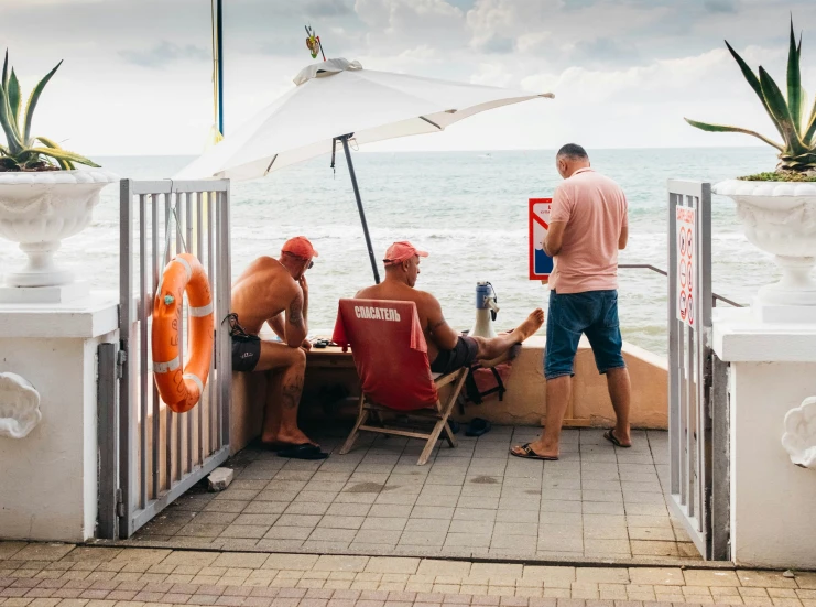three people sitting at an open white fence with an ocean view