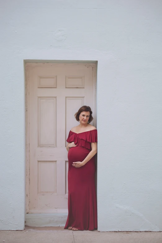 woman in off shoulder maroon dress leaning against a door