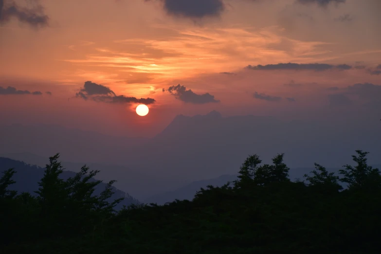 a sun setting over trees and mountains with trees