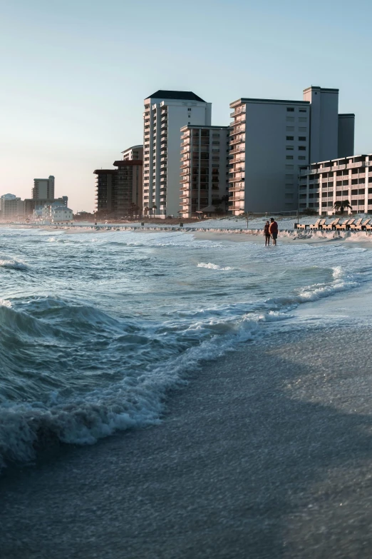 two people walk on the beach near a city skyline