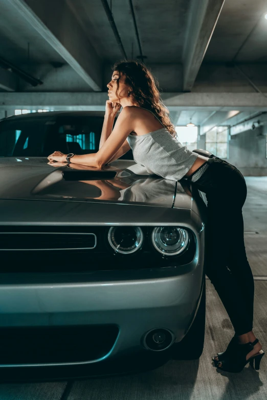woman leaning on the hood of a car in an underground parking lot