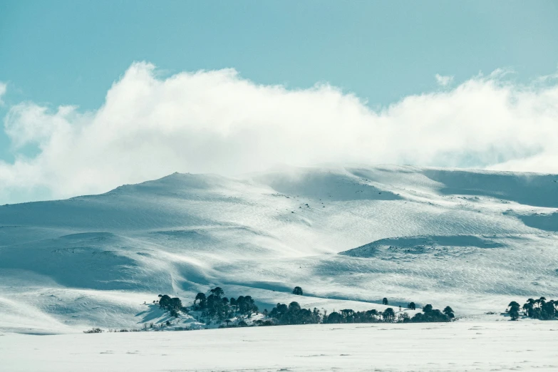 the sky is filled with clouds over the snowy hill