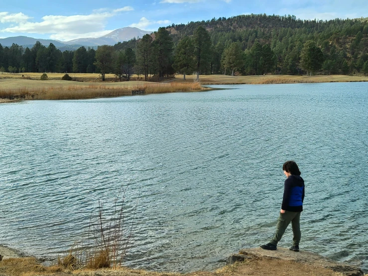 a woman in boots looks at the water and forest