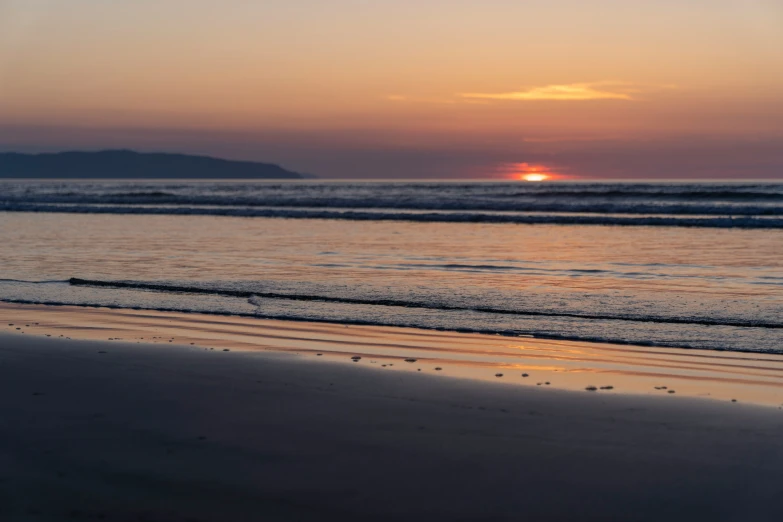 the sun is setting over the water on a beach