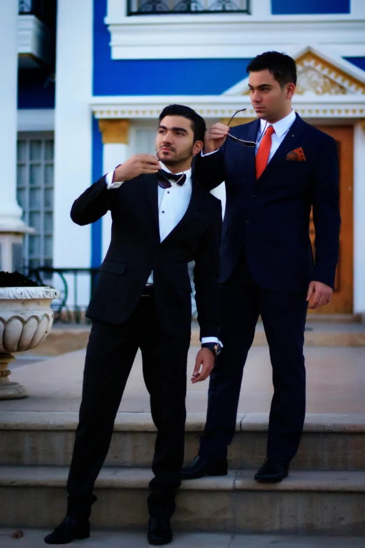 two men dressed in tuxedos and ties standing on some steps