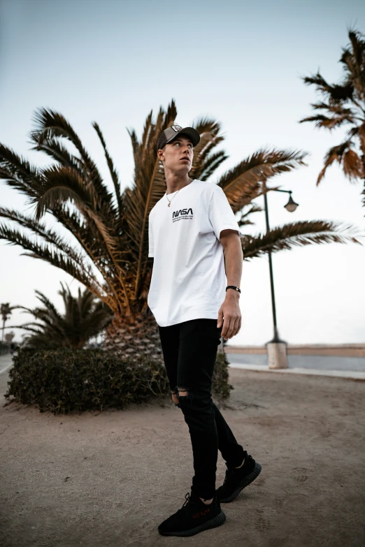 a man stands on the street wearing a white t - shirt and black pants